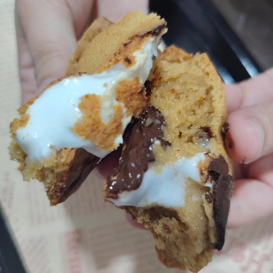 Freshly baked s'mores cookie pulled apart showing gooey marshmallow and melted chocolate